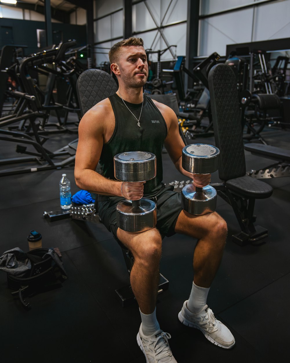 a man sitting in a gym holding two dumbs