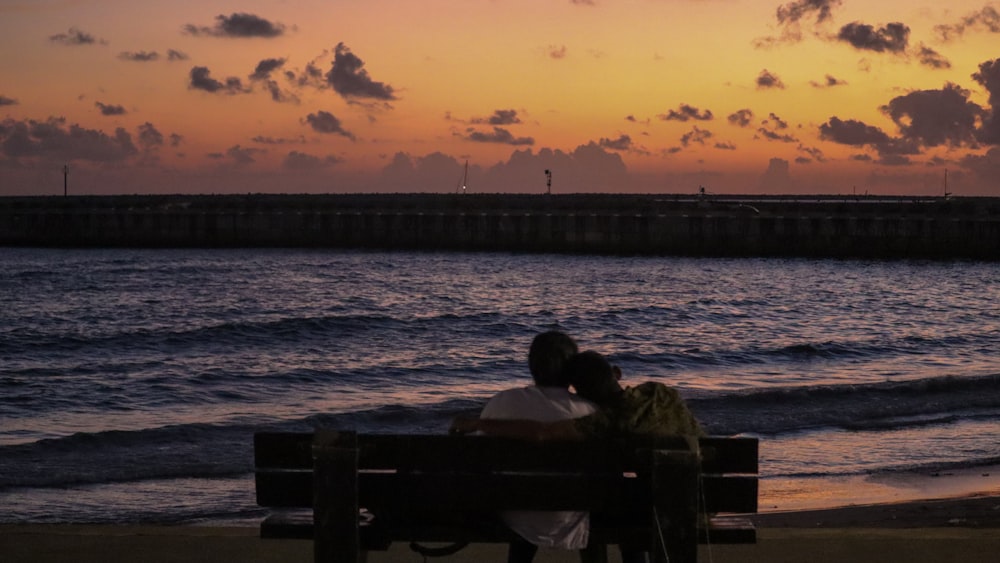 a couple sitting on a bench next to the ocean