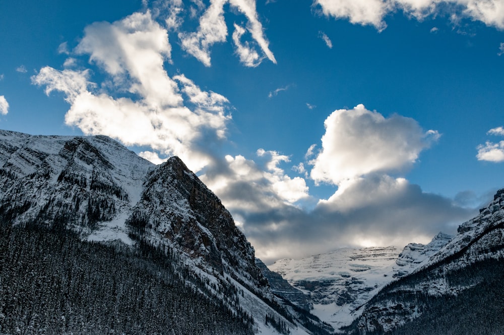 a snow covered mountain range under a cloudy blue sky