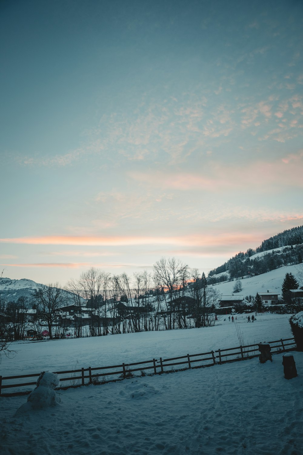 a snow covered field with a fence and mountains in the background