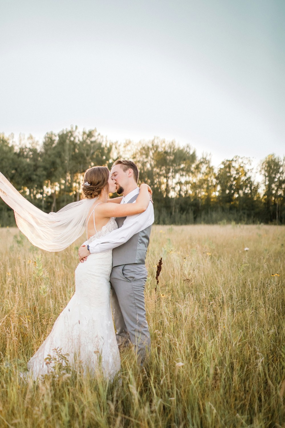 a bride and groom kissing in a field of tall grass