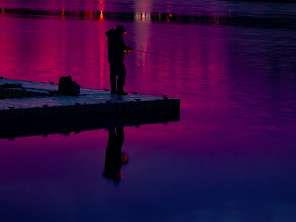 a man standing on a dock next to a body of water