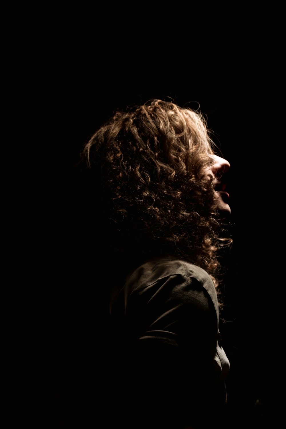 a man with curly hair standing in the dark