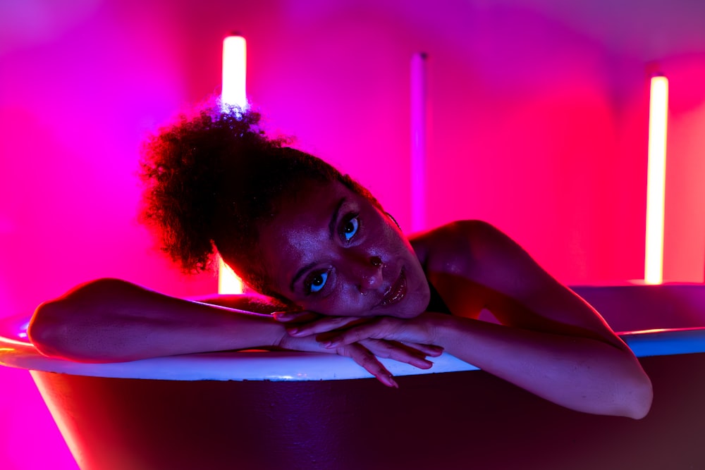 a woman laying in a bathtub in a pink light
