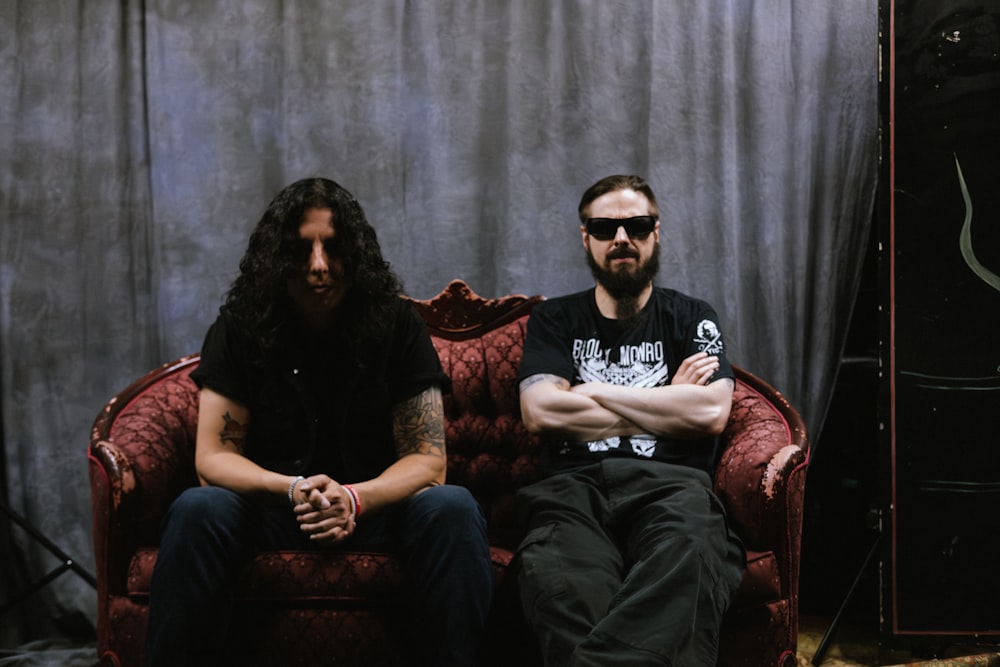 a couple of men sitting on top of a red couch