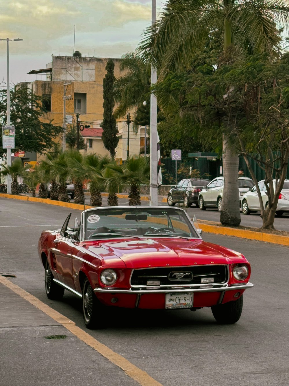 a red car driving down a street next to palm trees