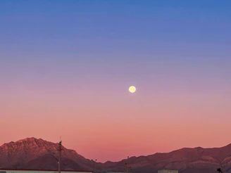 a full moon rising over a mountain range