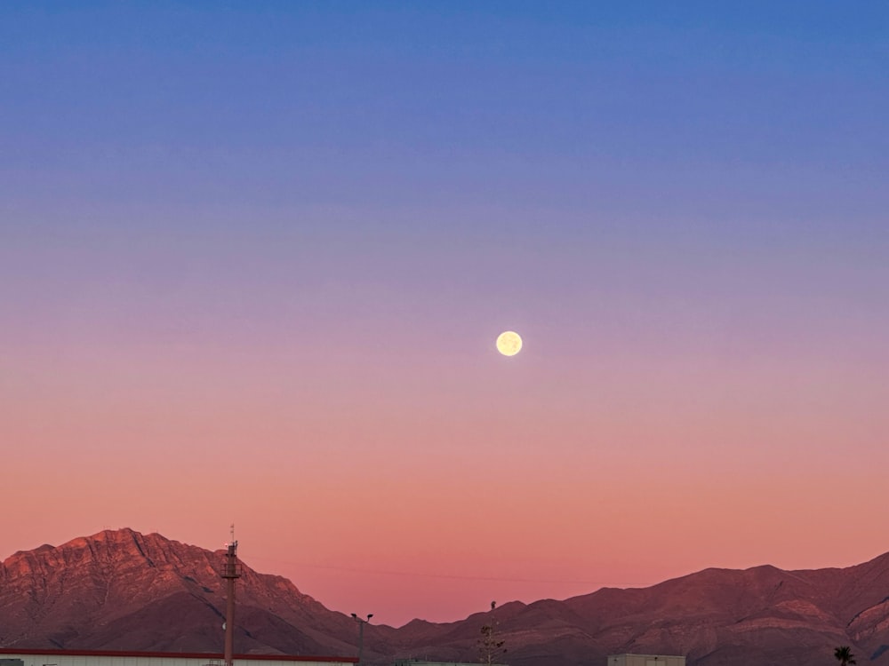 a full moon rising over a mountain range