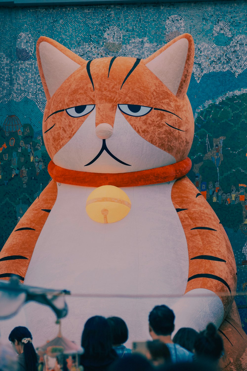 a large stuffed cat sitting in front of a crowd of people