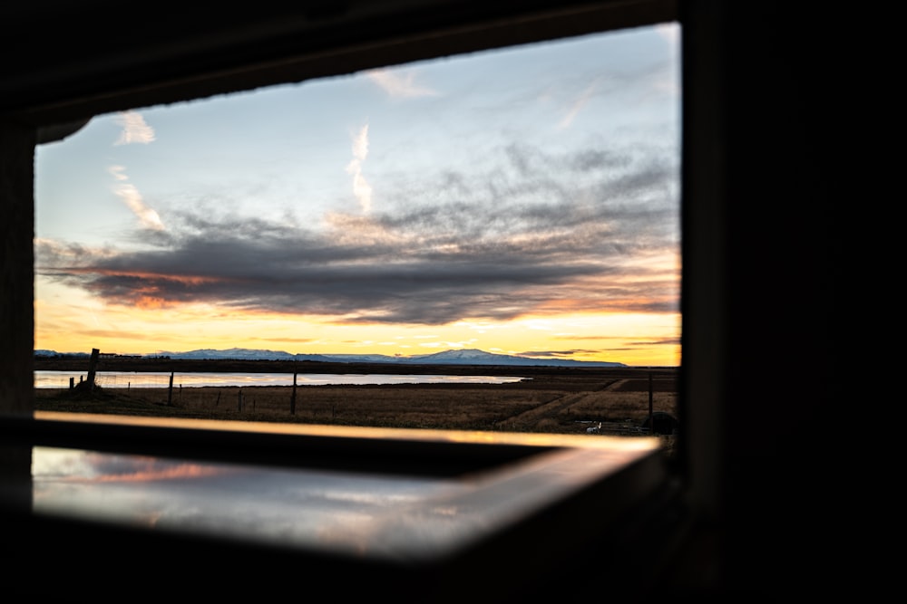 a window view of a lake and mountains at sunset