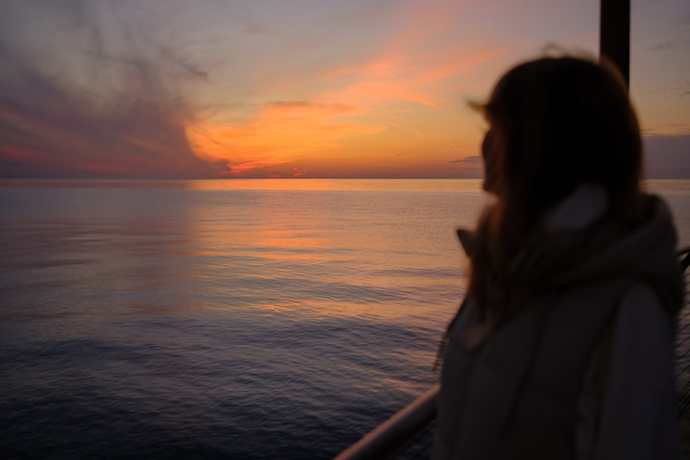 a woman looking out at the ocean at sunset