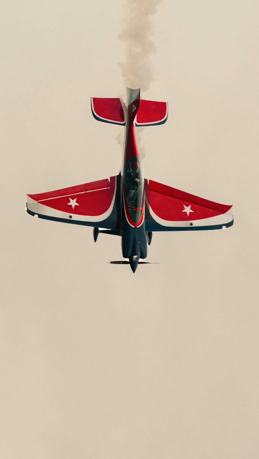 a red and white jet flying through a cloudy sky