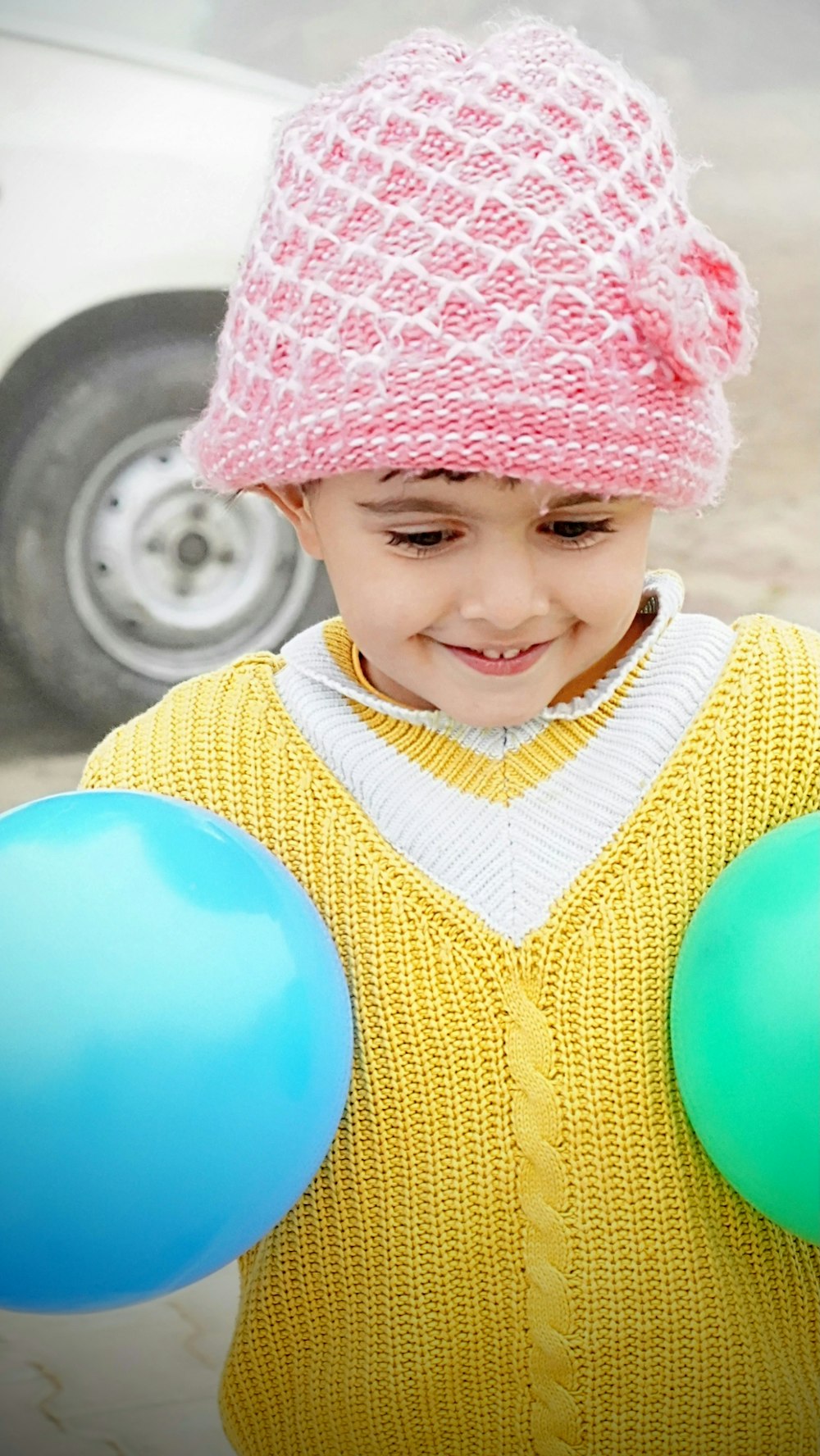 a young boy holding two balloons in front of a car