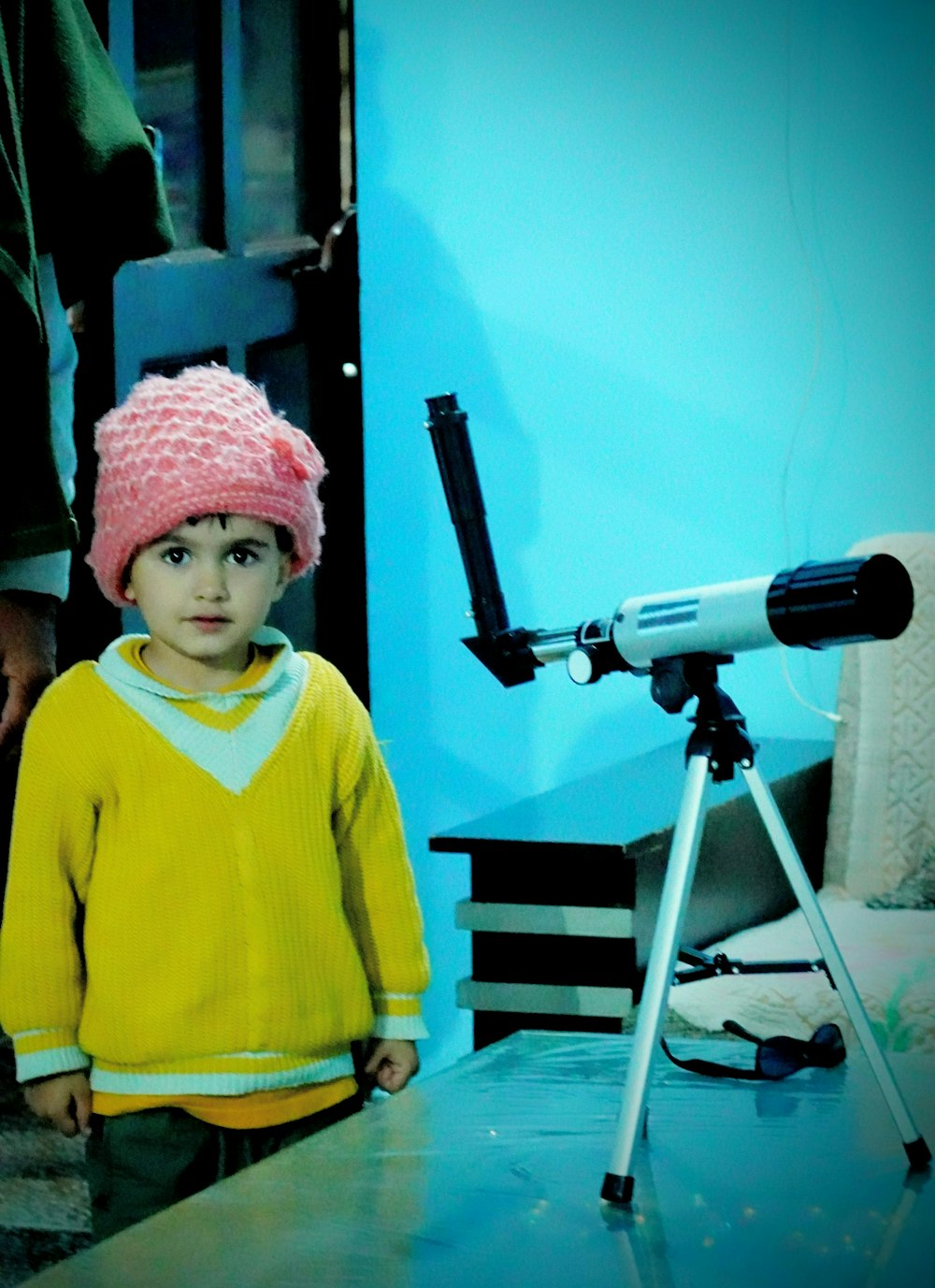a young boy wearing a pink hat standing in front of a telescope