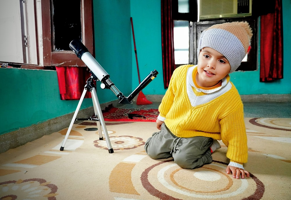 a young boy sitting on the floor in front of a telescope