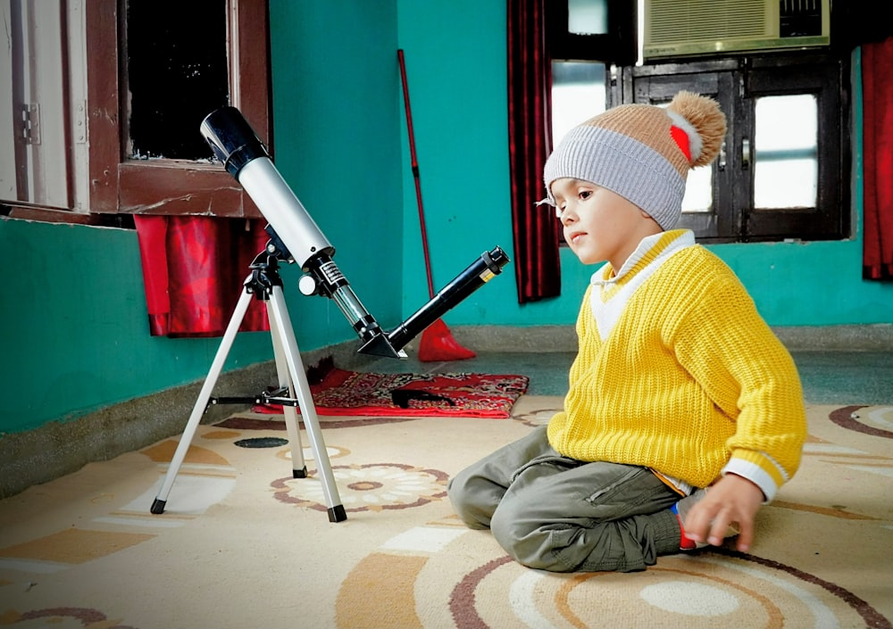 a young boy sitting on the floor next to a telescope