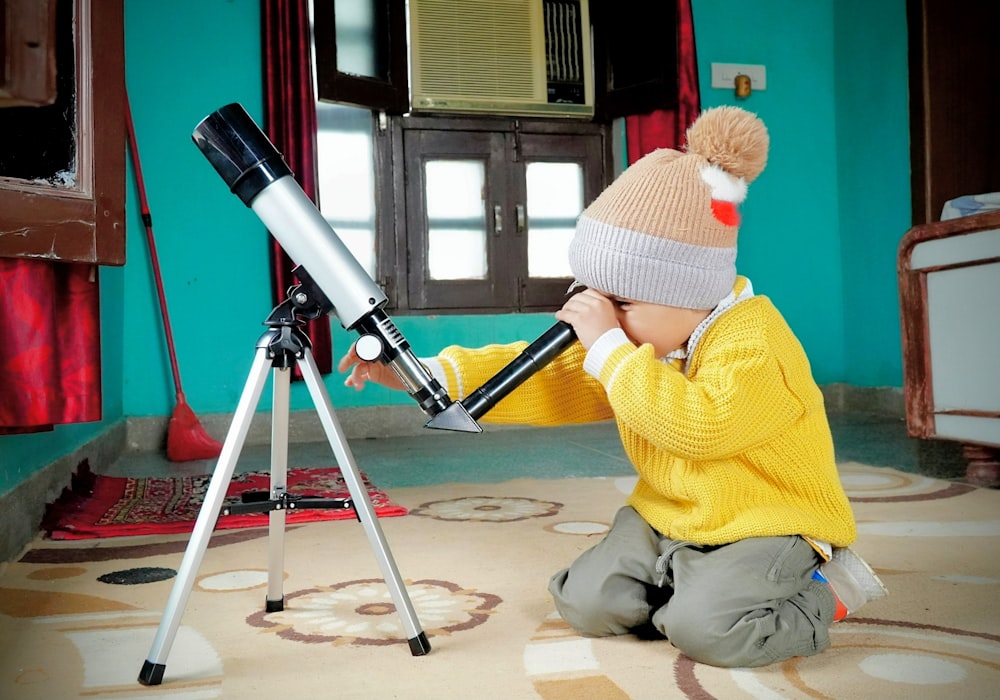a little boy sitting on the floor looking through a telescope