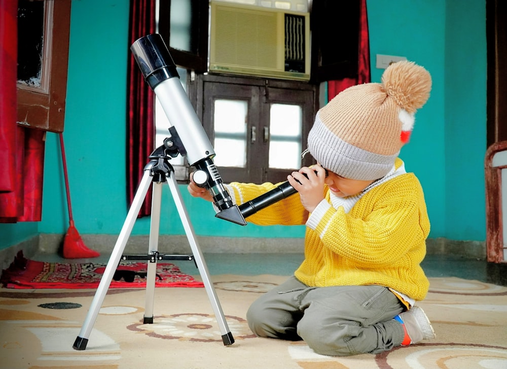 a little boy sitting on the floor looking through a telescope