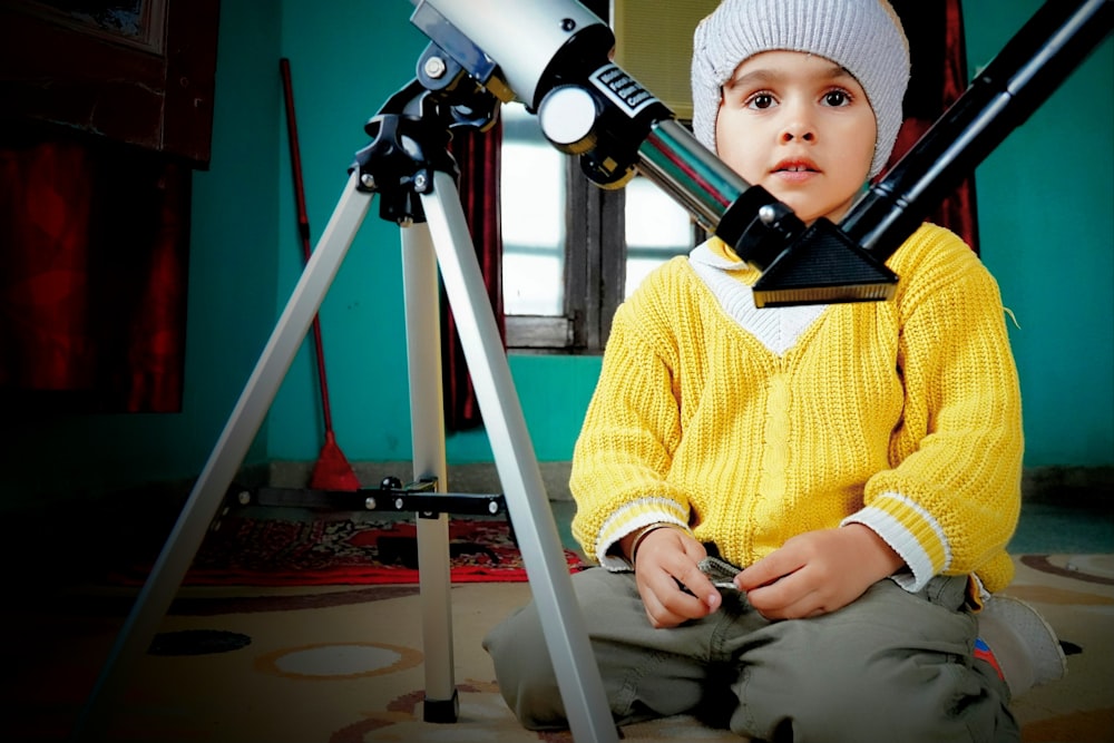 a young boy sitting in front of a telescope