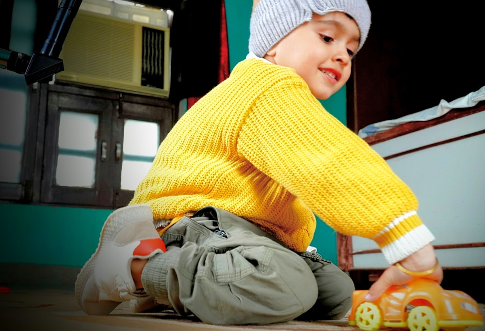 a little boy sitting on the ground playing with a toy car