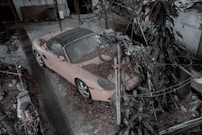 a pink car parked in a yard next to a tree