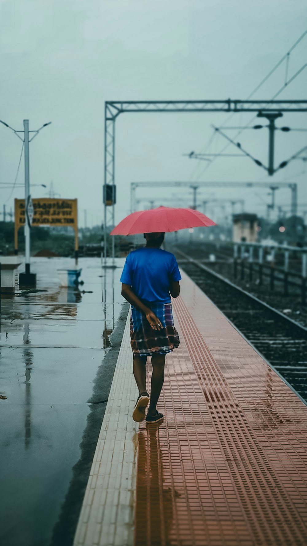 ein Mann, der mit einem roten Regenschirm ein Bahngleis entlanggeht