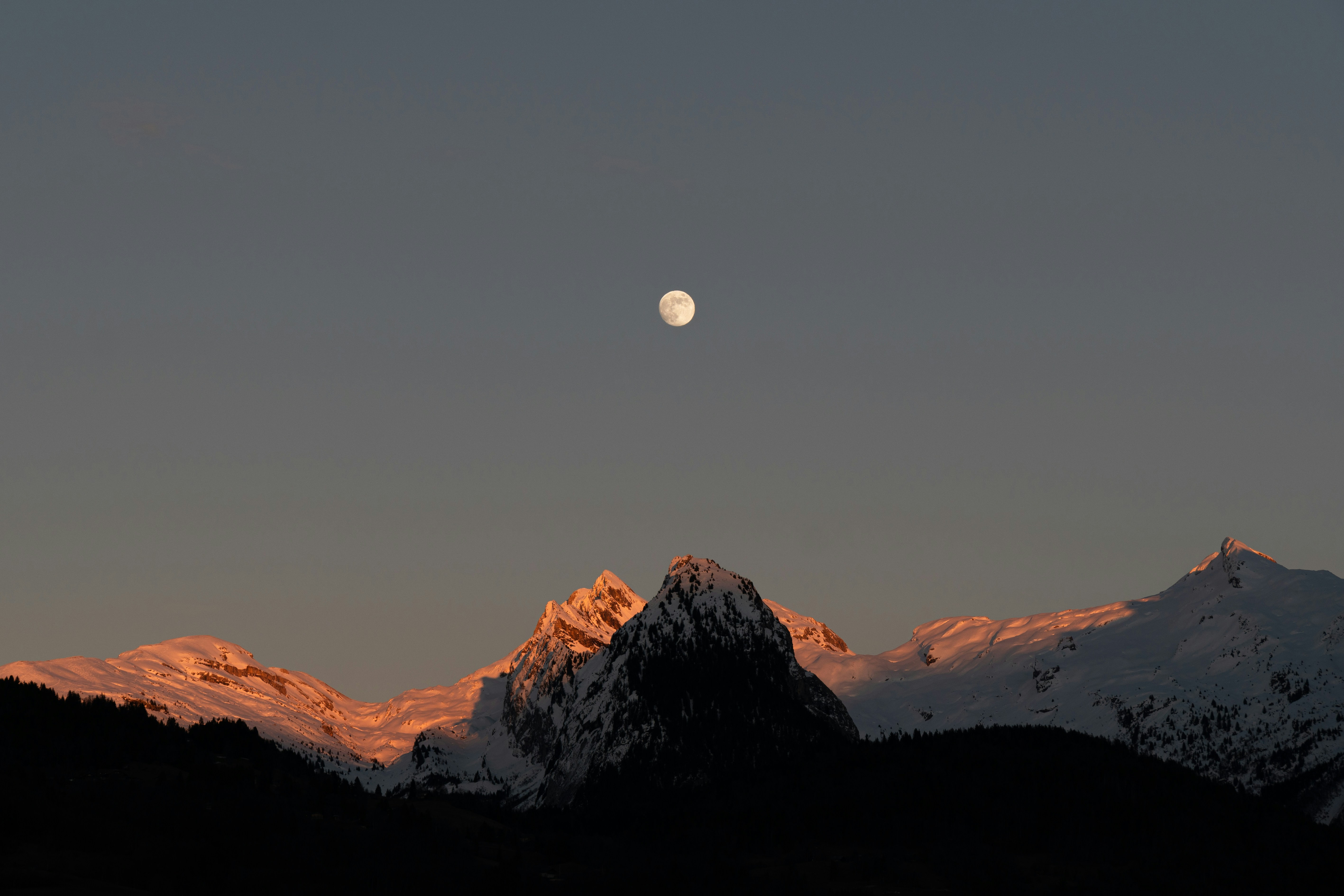 the moon is setting over a mountain range