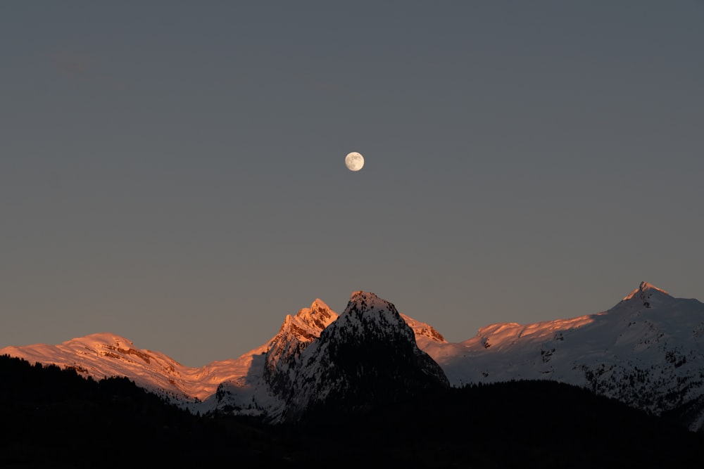 the moon is setting over a mountain range