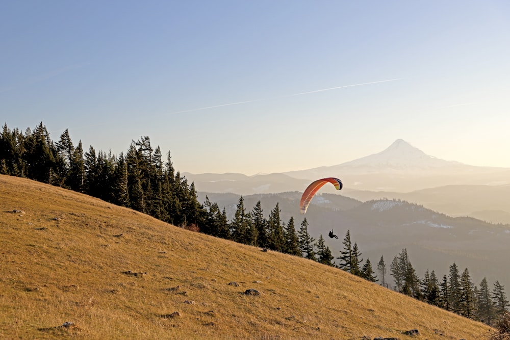 a paraglider is flying over a grassy hill