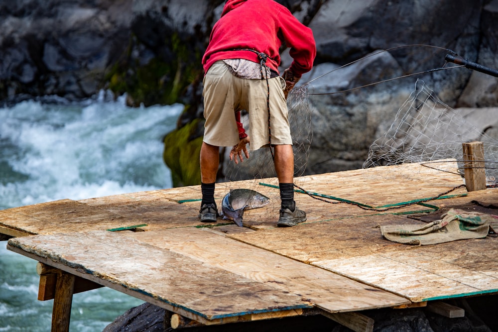 a man standing on top of a wooden platform next to a river