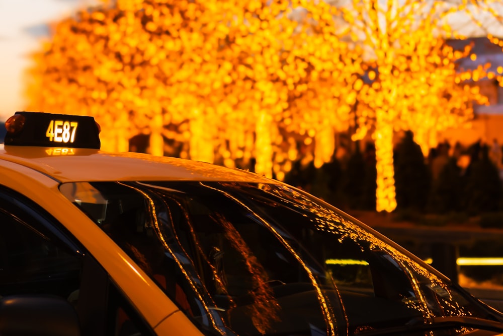 a yellow taxi cab is parked in front of a row of trees