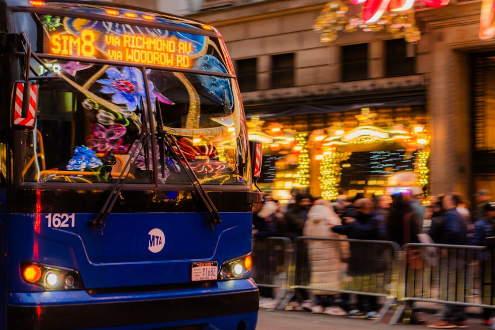 a blue bus driving down a street next to a crowd of people