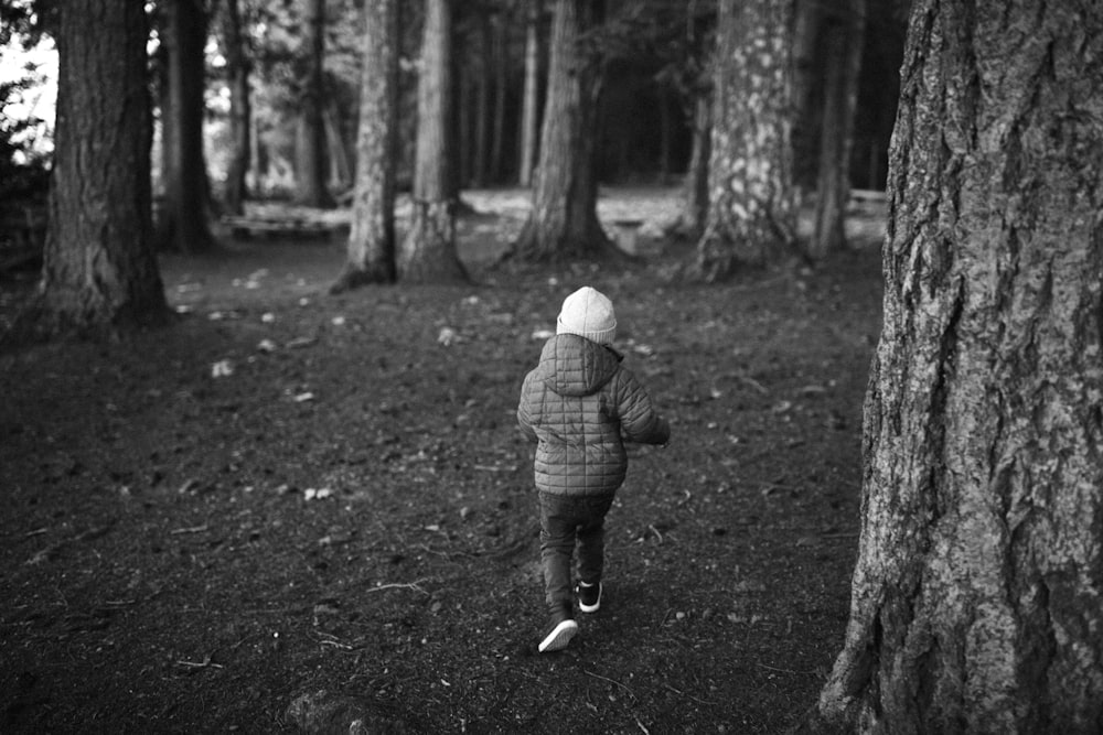 a little boy walking through a forest next to a tall tree
