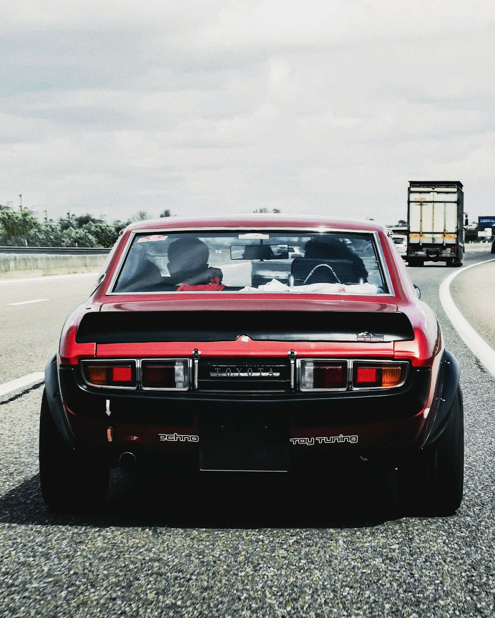 a red car driving down a road next to a truck