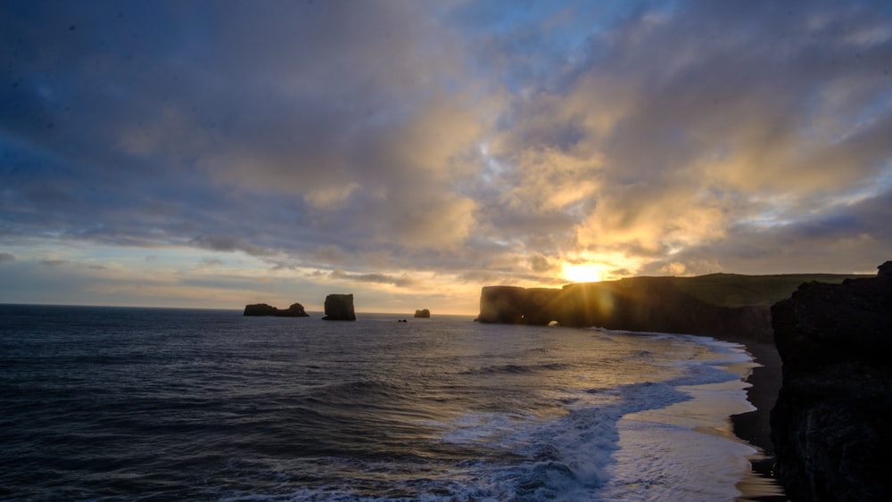 the sun is setting over the ocean with cliffs in the background