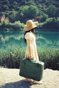 a woman in a hat carrying a green suitcase
