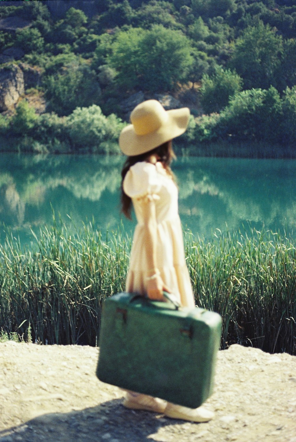 a woman in a hat carrying a green suitcase