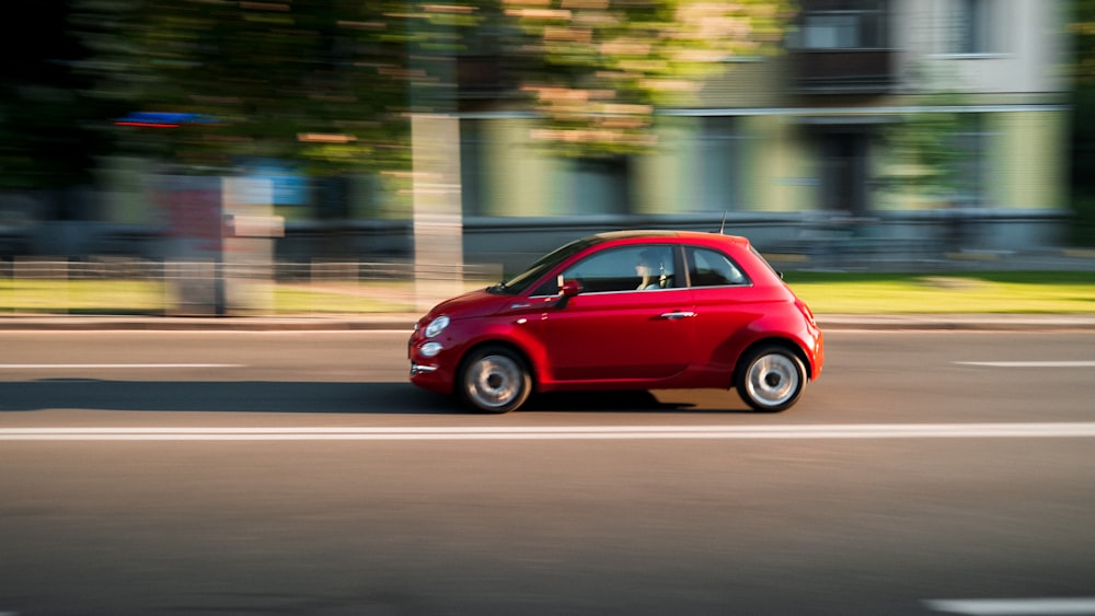 a small red car driving down a street