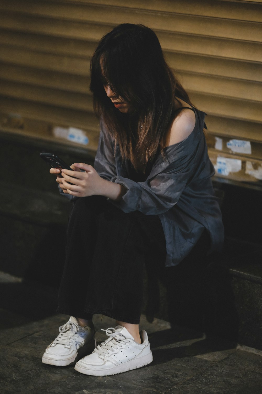 une femme assise sur le sol en train de regarder son téléphone portable