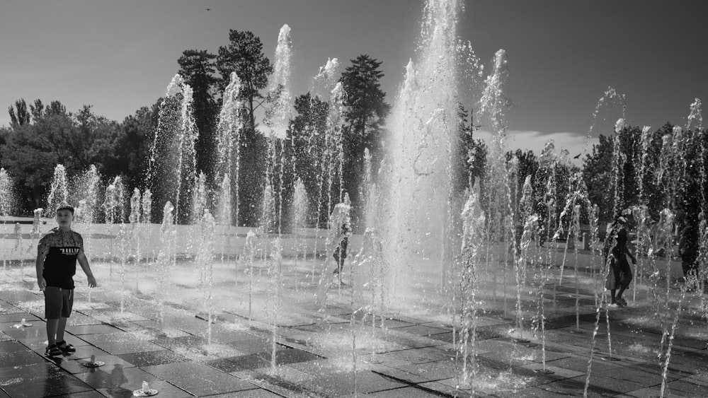 a black and white photo of a man standing in front of a fountain