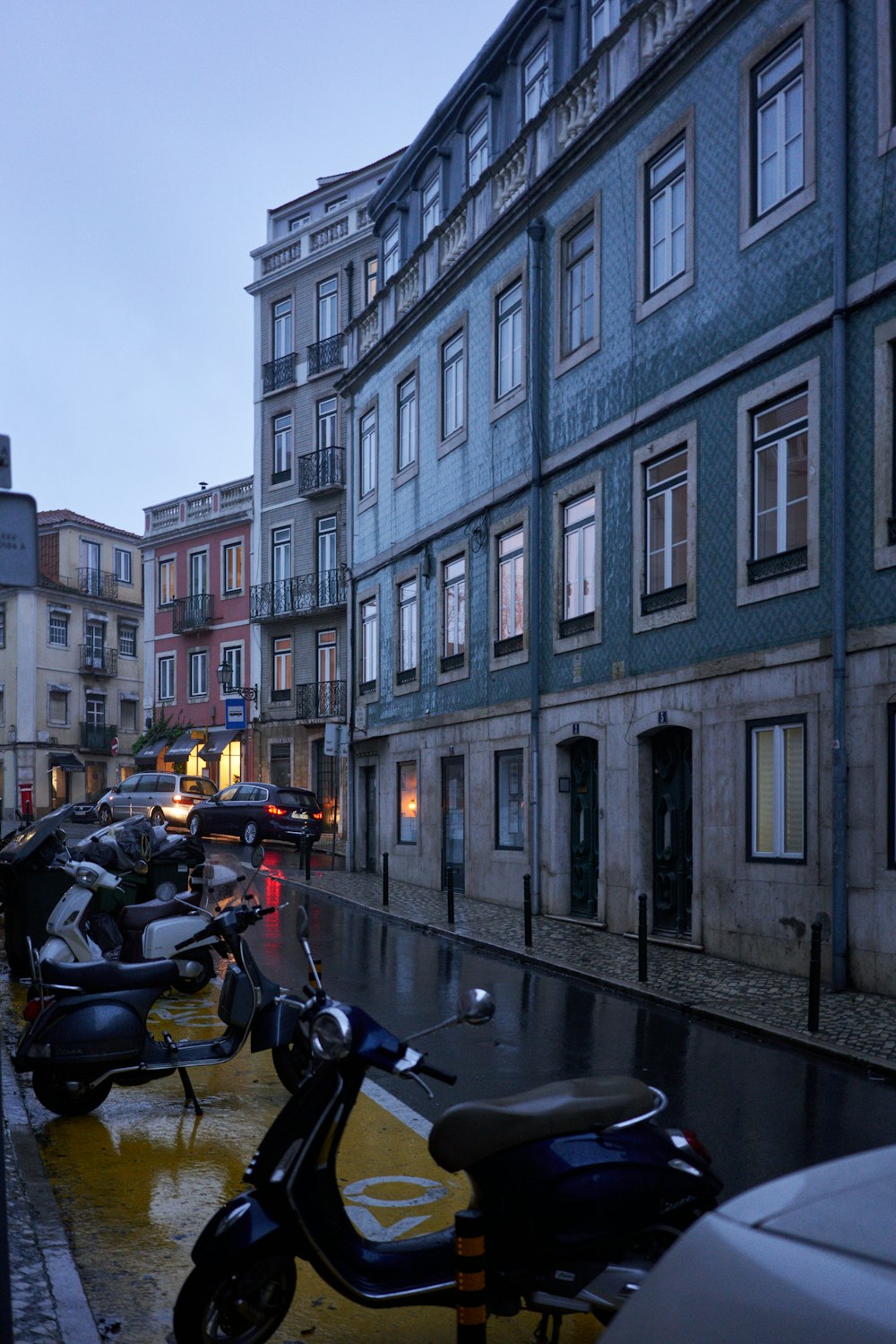 a row of parked motor scooters on a wet street