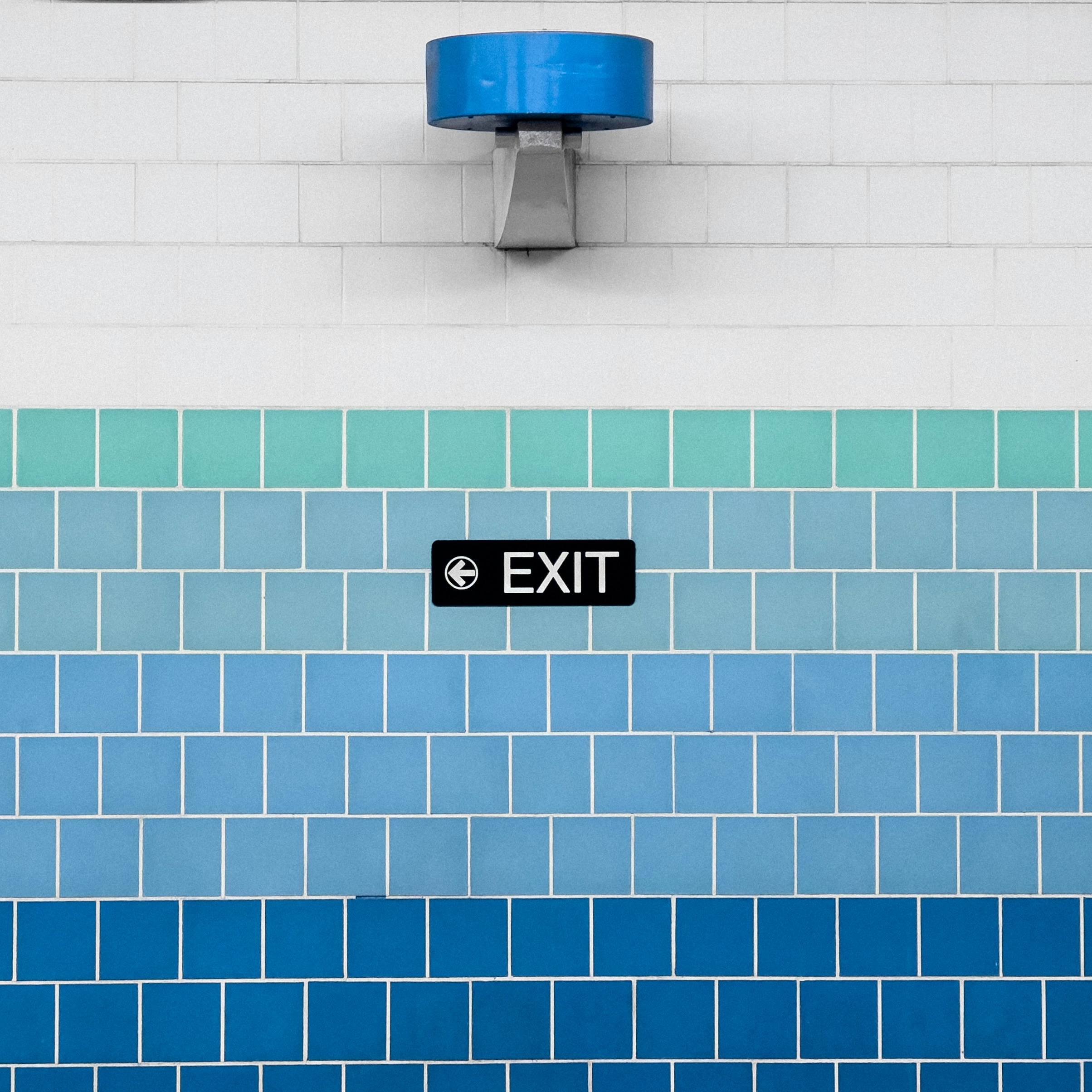un mur carrelé bleu et blanc avec un panneau de sortie