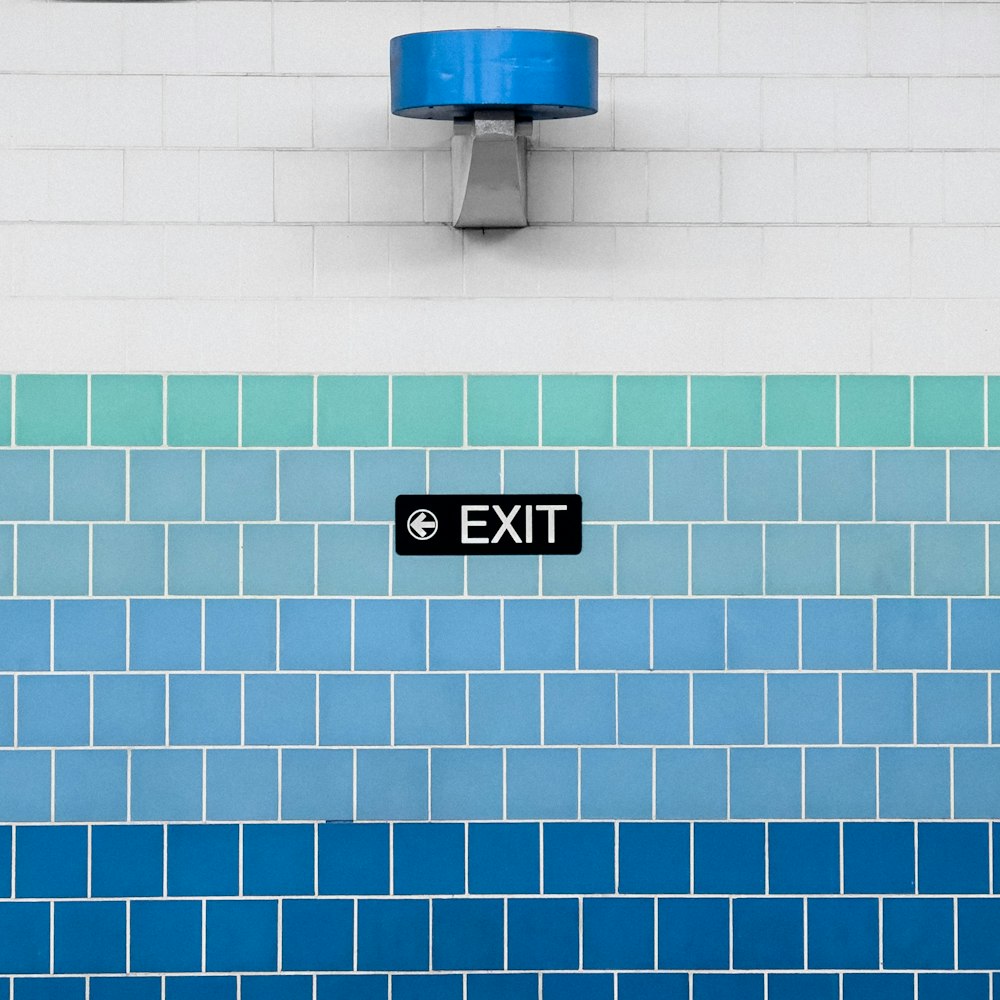 una pared de azulejos azules y blancos con una señal de salida
