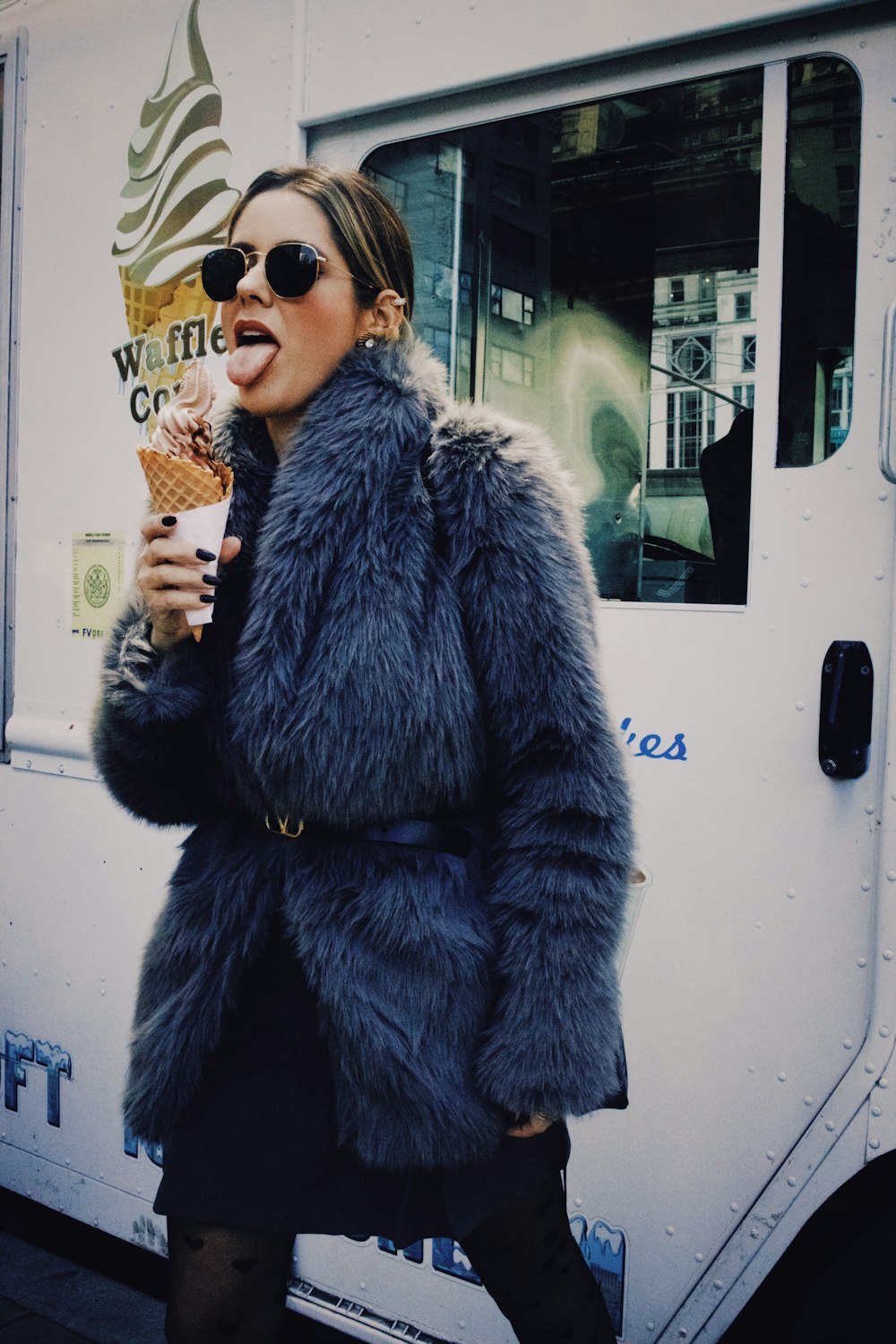 una donna in una pelliccia che mangia un cono gelato