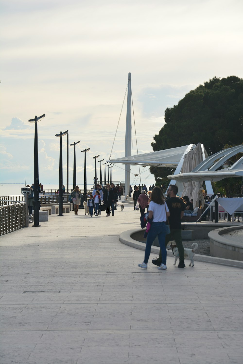 a group of people walking down a sidewalk next to a body of water