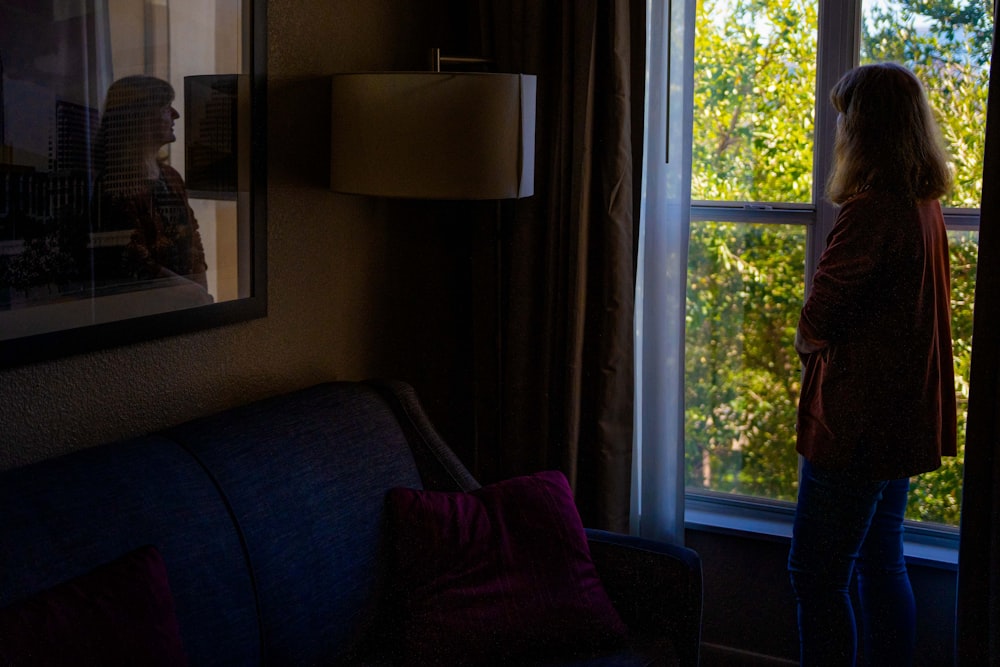 a woman standing in front of a window next to a couch