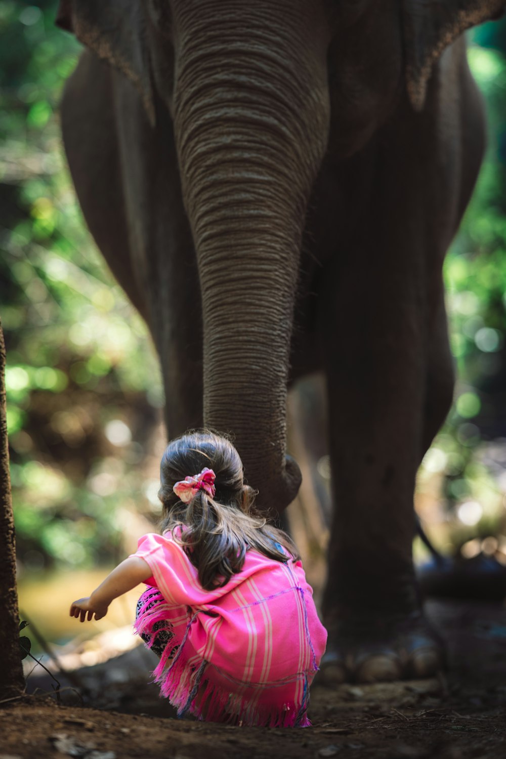 a little girl sitting on the ground next to an elephant