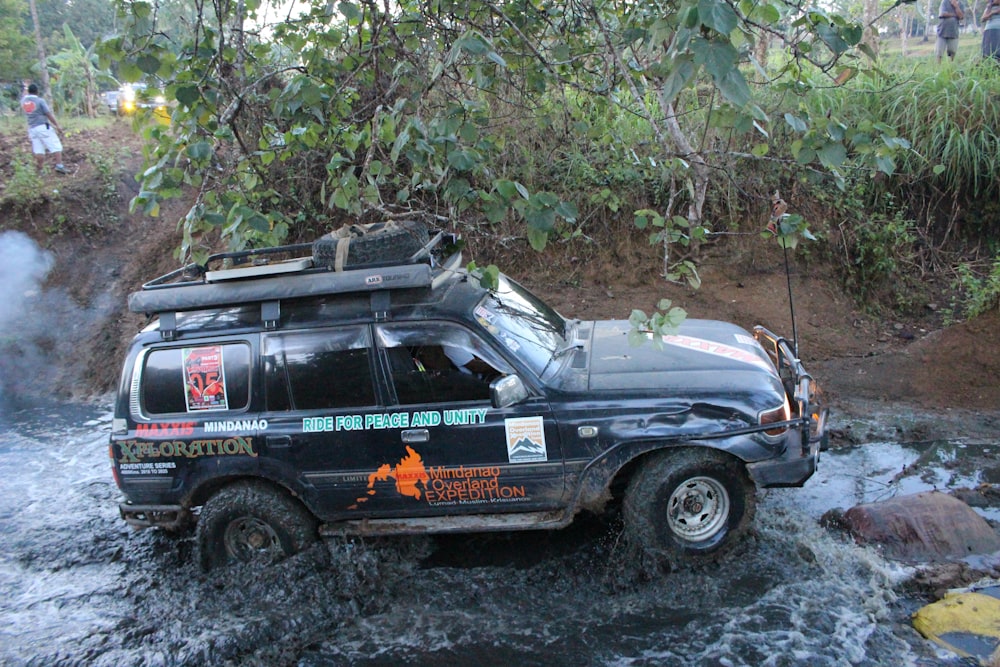 a black truck driving through a river next to a forest