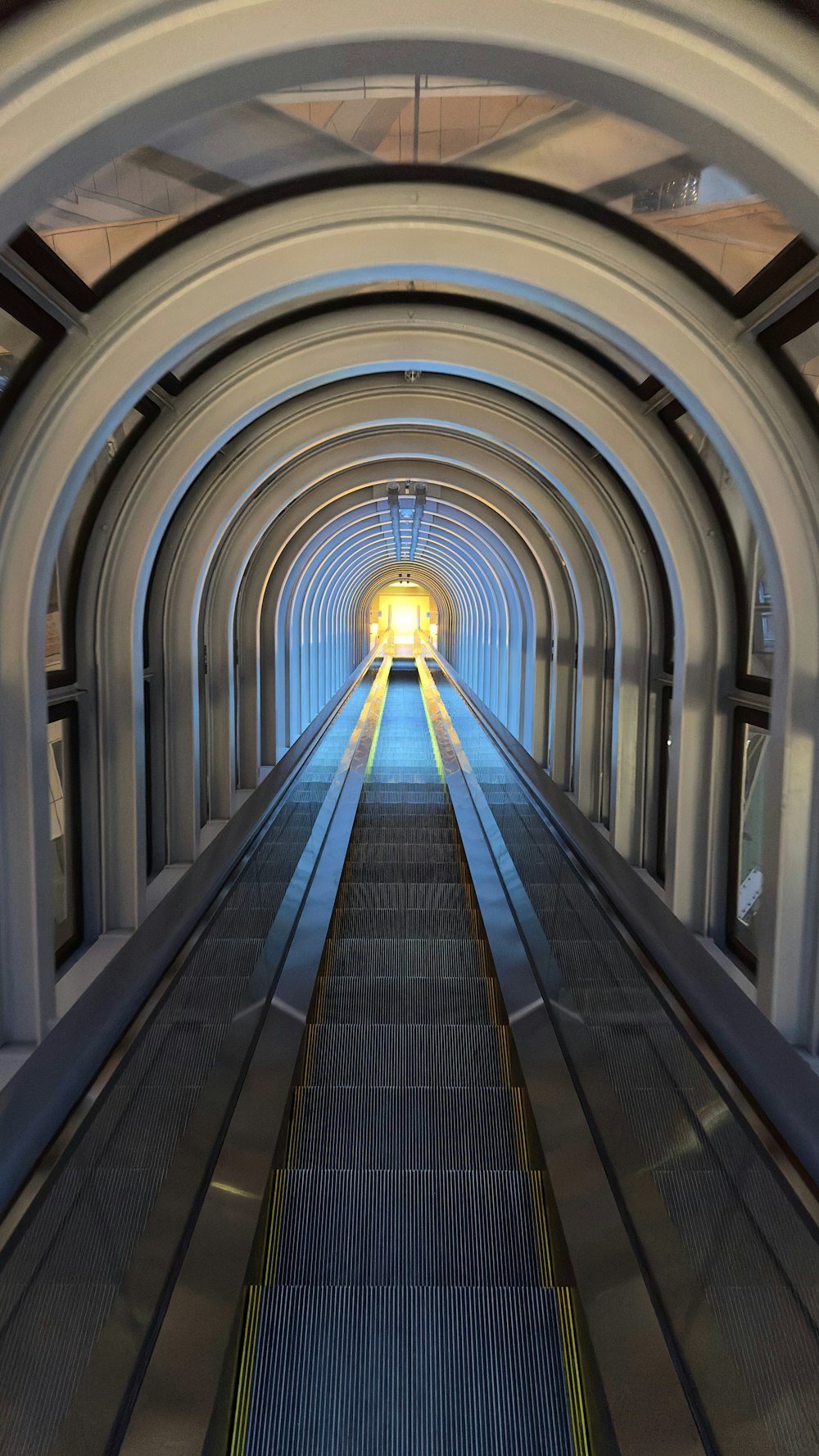 an escalator going down a tunnel with a light at the end