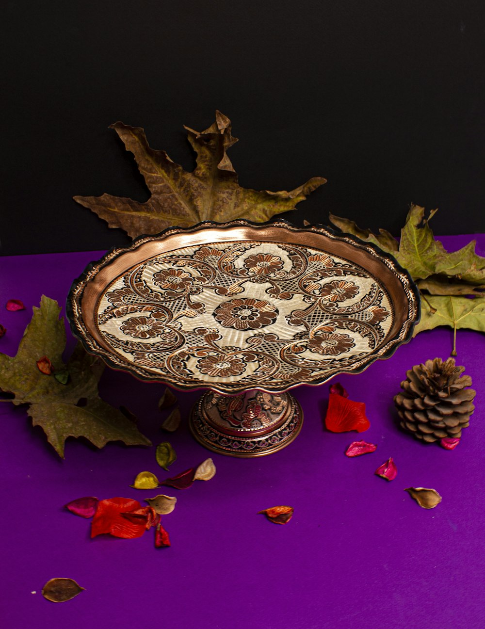 a decorative bowl with leaves and a pine cone on a purple surface